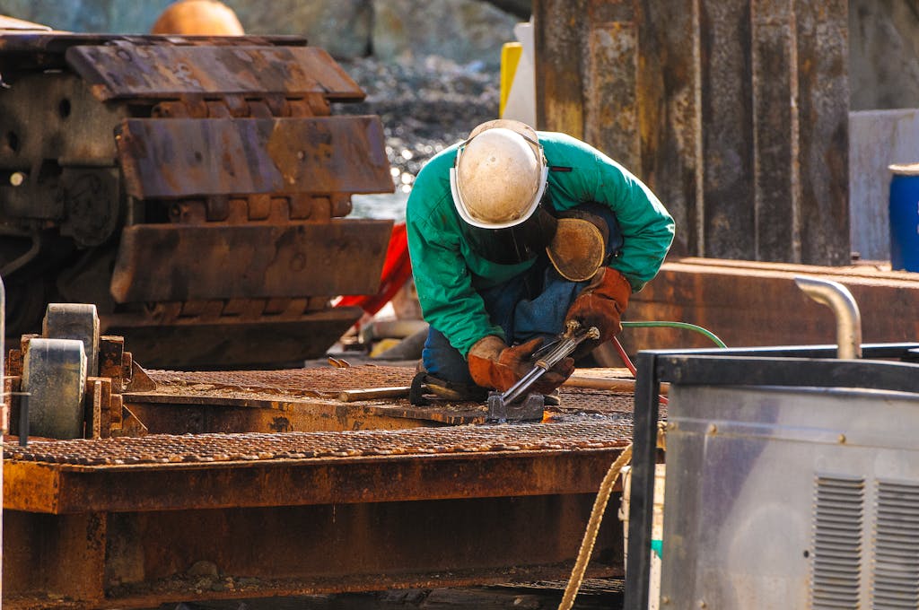 A welder in protective gear works at a construction site outdoors.